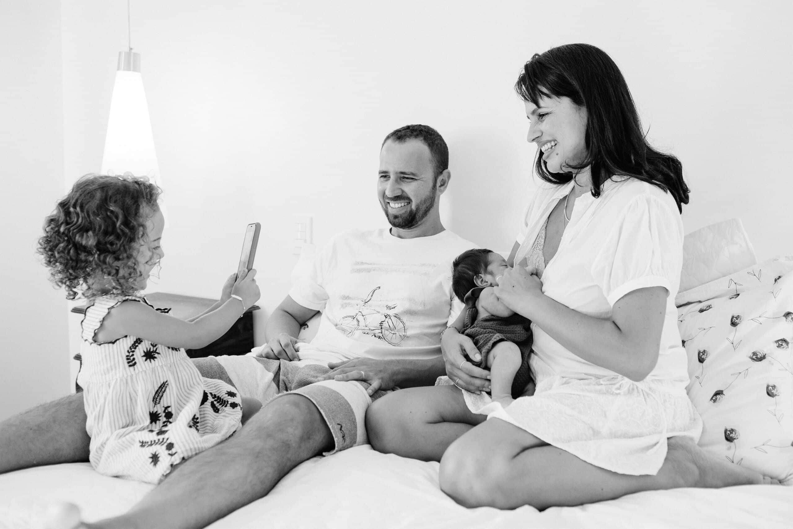 A family recording their newborn son while breastfeeding